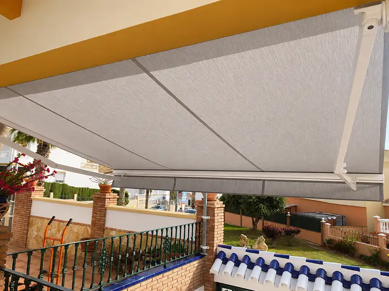 Toldo articulado con lona gris extendido en una terraza