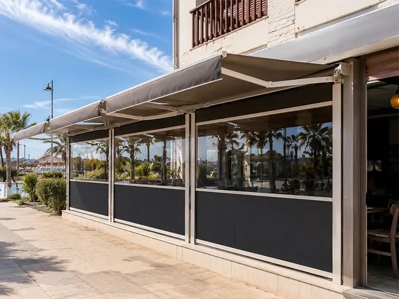 Toldo cortavientos con guías y toldo articulado en la terraza de un restaurante