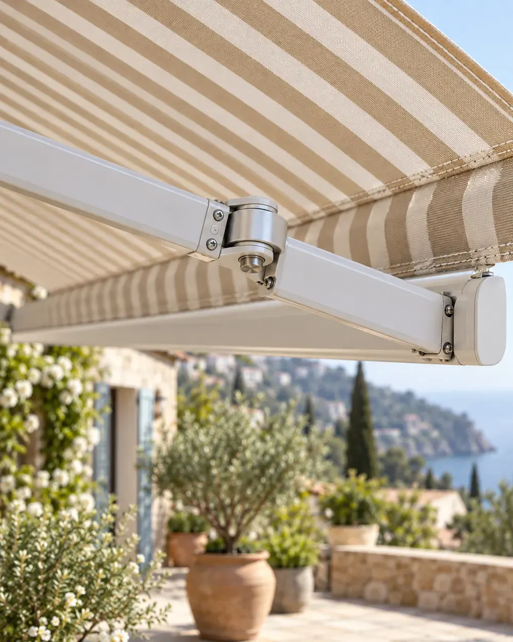Brazo articulado de un toldo a medida Brazo articulado de aluminio blanco y lona de rayas beige de un toldo a medida en una terraza con vistas al mar