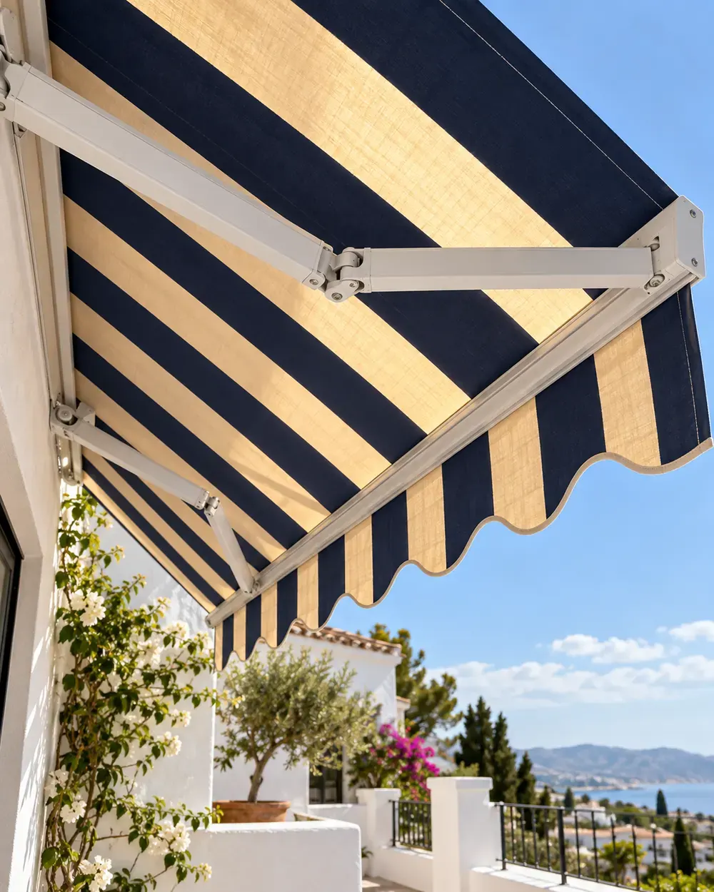 Brazos y lona de un toldo articulado Brazos articulados de aluminio blanco y lona de rayas azul marino y arena de un toldo articulado vistos desde abajo