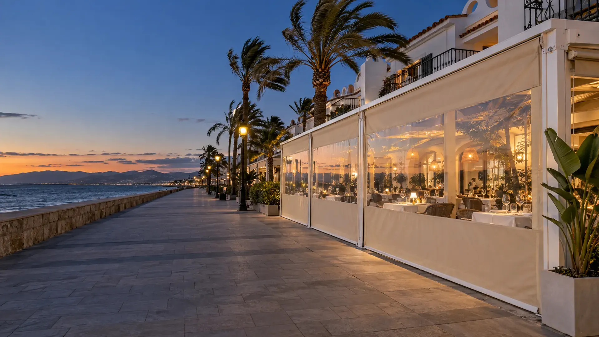 Toldo cortavientos en Málaga Toldo cortavientos en Málaga: cortavientos con guías y ventana transparente cerrando la terraza de un restaurante en el paseo marítimo